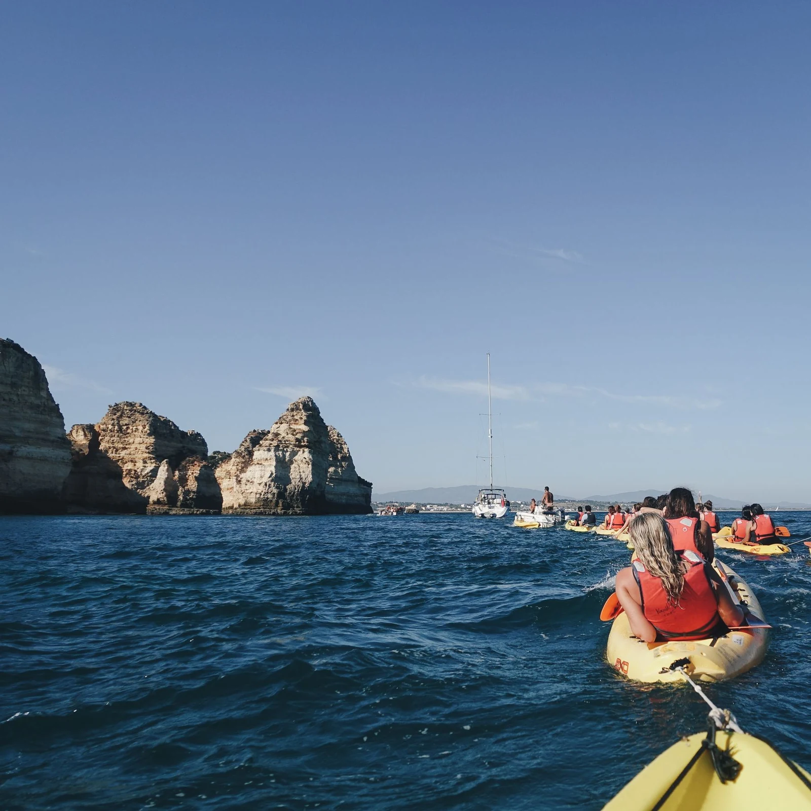 A group kayaking together beside coastal cliffs under a clear blue sky