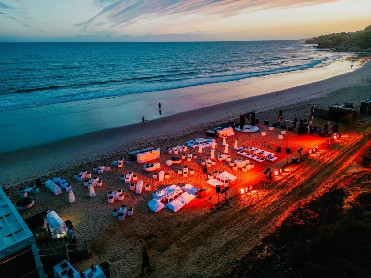 Beach event at Pine Cliffs with tables and red-lit hospitality areas beside the ocean after sunset.