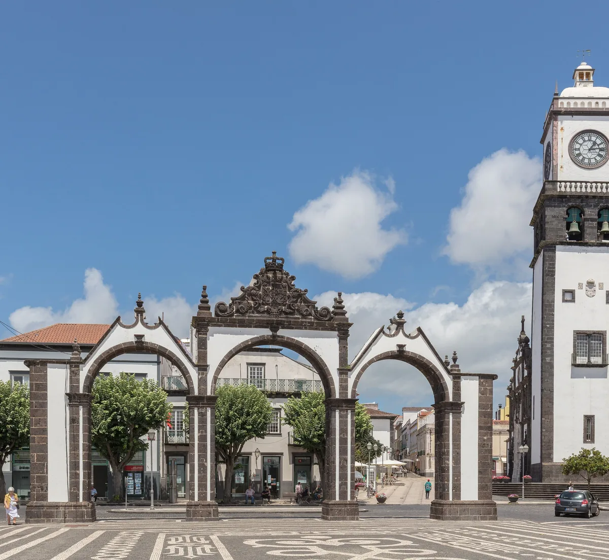 The three arches of Portas da Cidade in Ponta Delgada, with a church tower beyond.