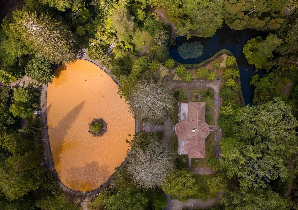 An aerial view of the amber thermal pool surrounded by trees at Parque Terra Nostra.