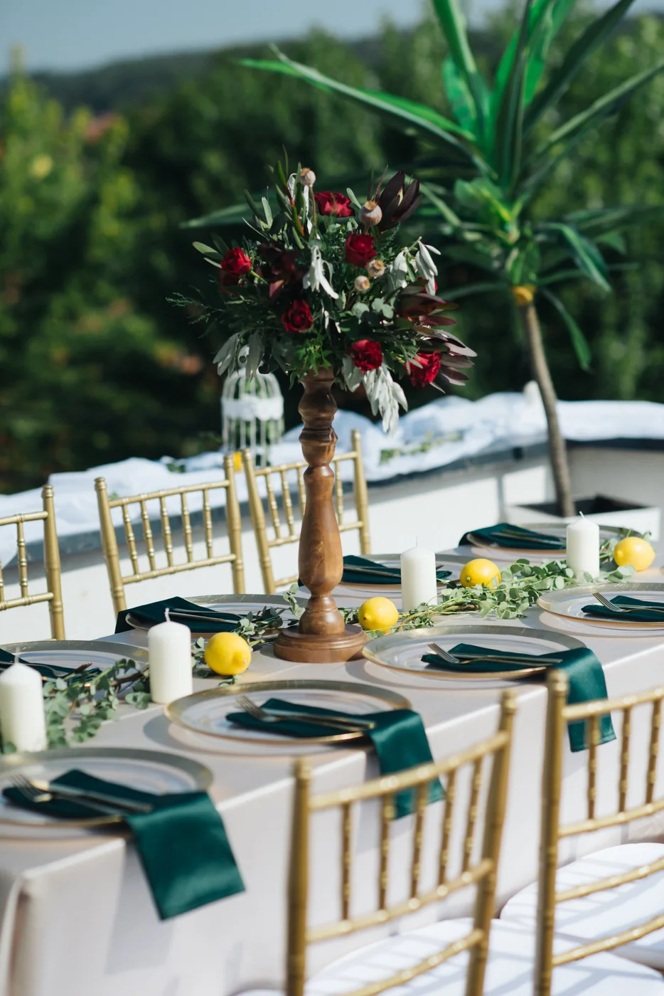 An outdoor wedding table with flowers, fruit, glasses and white chairs.